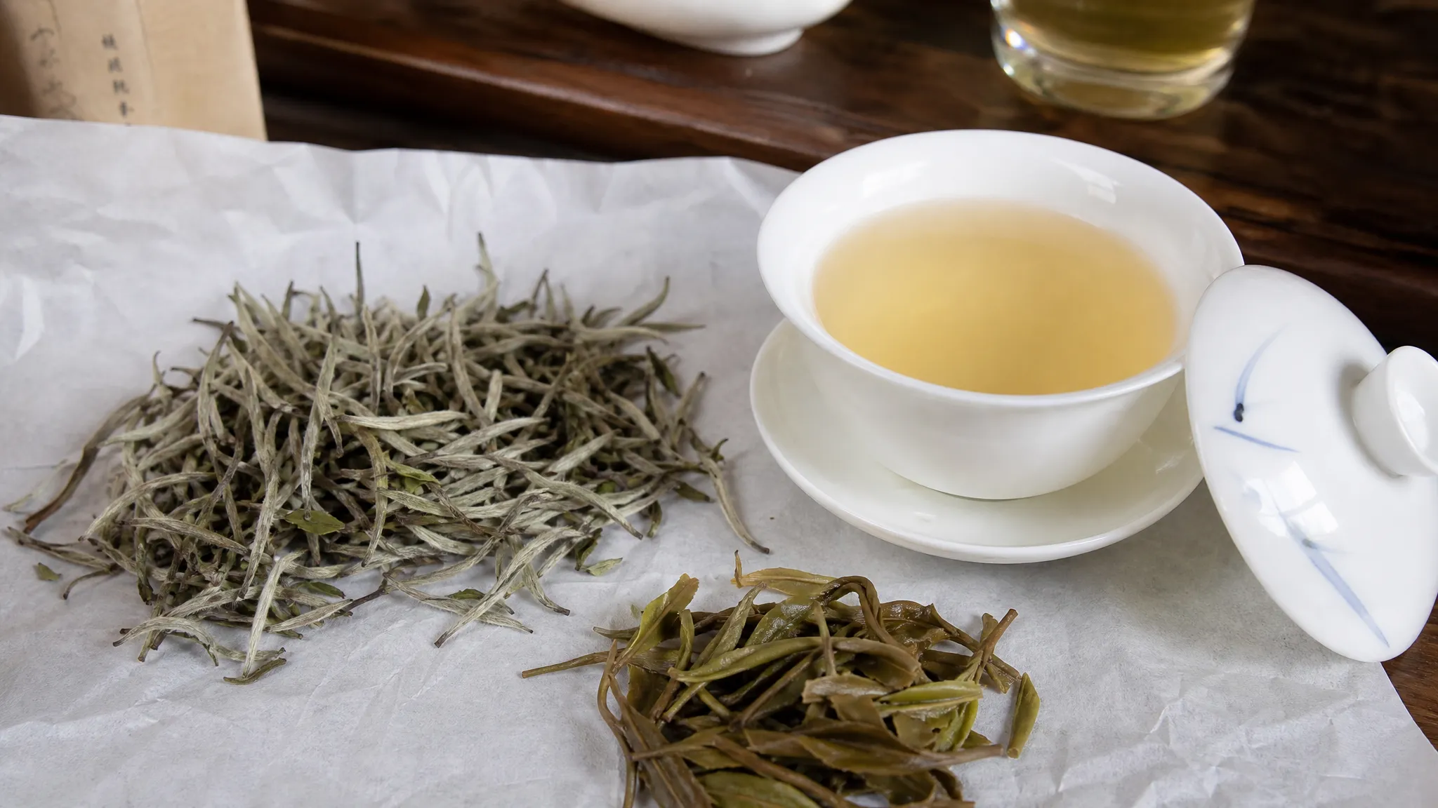 White tea buds, gaiwan, and pale liquor on a tasting table for whiteteaaura